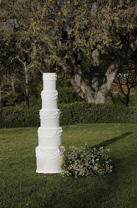Wedding cake five tier wedding cake with white frosting and piped scallop icing, styled with greenery and small white flowers on a garden lawn