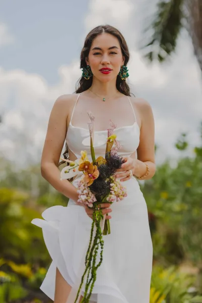Bridal portrait of a bride in a strapless white satin wedding dress holding a cascading bouquet, framed by palm trees and blue sky