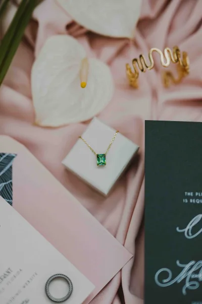 Invitation suite wedding flat lay with pink envelope, black and white cards, ring, pendant necklace, calla lily on soft pink satin backdrop