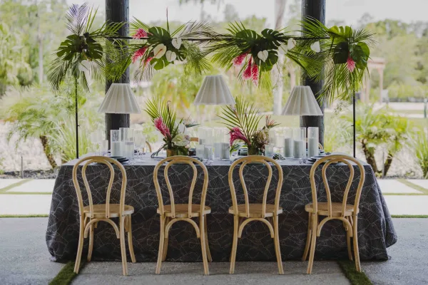 Reception tablescape with tropical wedding tablescape greenery runner, monstera and anthurium blooms, candles and lamps on a covered patio
