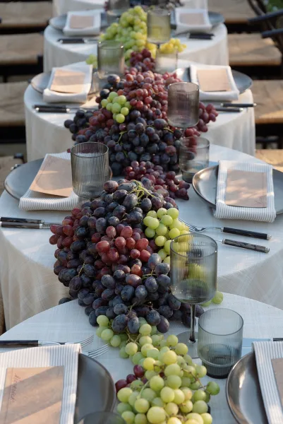 Reception tablescape with grape table runner, gray plates, striped napkins, menu cards, ribbed tumblers and smoked glasses on an outdoor table