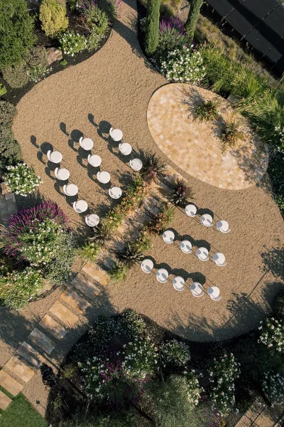 Ceremony setup with outdoor ceremony seating in a semicircle of white chairs around a stone paver platform, greenery and florals lining the aisle