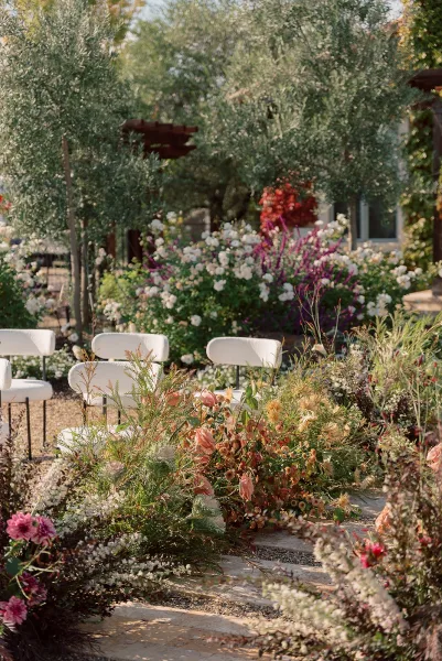 Ceremony aisle decor with outdoor ceremony aisle flowers, white chairs and lush ground floral arrangements along a garden patio setting
