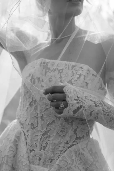 Bridal dress detail with lace wedding dress bodice and strapless neckline, tulle veil draped over hand showing engagement ring in soft light