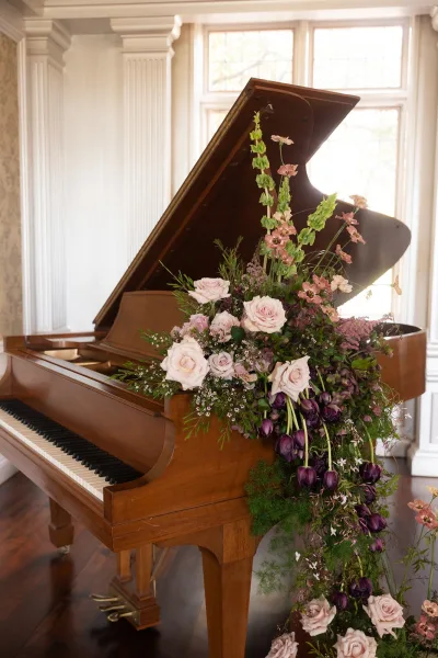 Piano floral arrangement cascades as grand piano wedding flowers, with blush roses by tall windows and white columns in a classic room