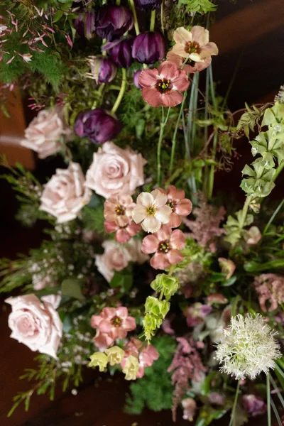 Floral arrangement of wedding florals, featuring lush roses in an airy, asymmetrical mix, resting on a wood surface.