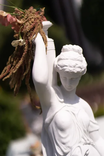 Statue decor with a floral draped statue, blooms cascading over a white figure amid garden greenery for refined outdoor wedding styling.