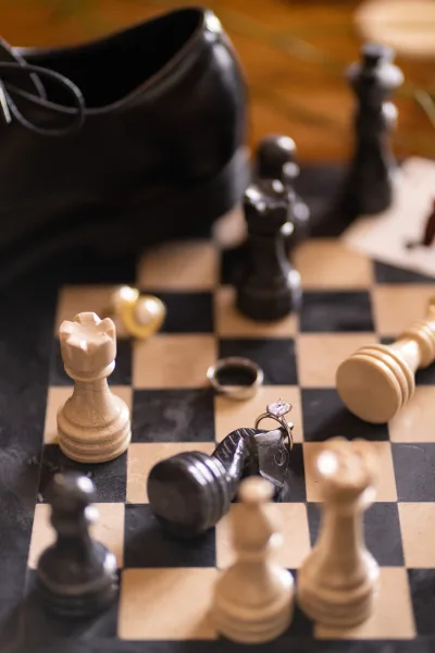 Wedding ring detail in a ring flatlay with a solitaire engagement ring and men's wedding band styled on a chessboard.