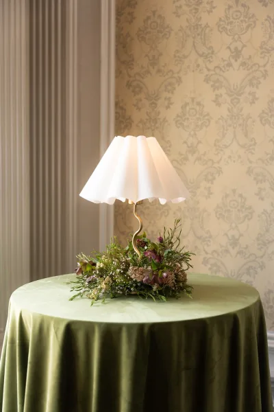 Wedding centerpiece, a lamp centerpiece with a pleated lampshade set against patterned wallpaper and fluted wall panels.