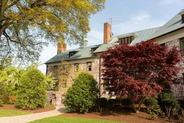 Wedding venue exterior with a brick facade, a garden wedding venue framed by trees and shrubs beside a neat lawn under a blue sky.