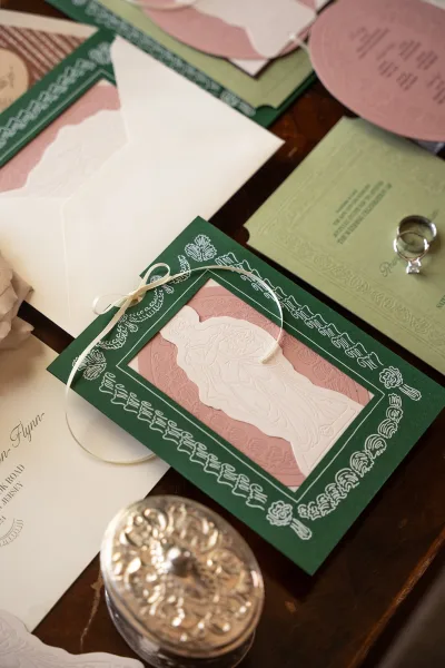 Invitation suite of letterpress wedding invitations with wedding rings on a wood table, showcasing crisp type and textured paper.