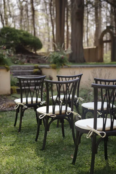 Ceremony seating with outdoor ceremony chairs in neat rows, black chairs with white cushions and ribbon ties on a garden lawn near stone steps