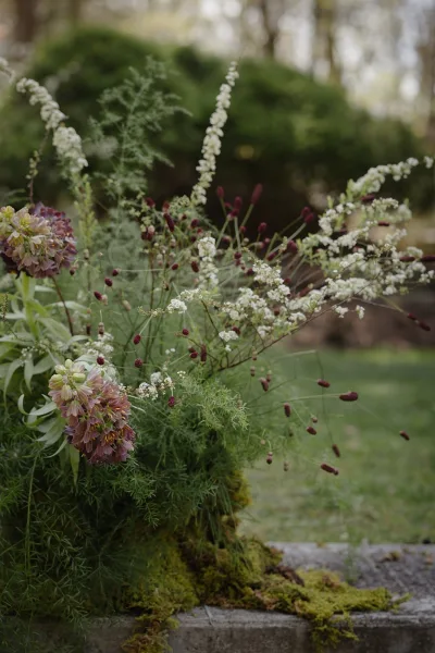 Wedding floral arrangement with garden wedding flowers, featuring wildflowers and burgundy stems on stone steps in a leafy garden setting