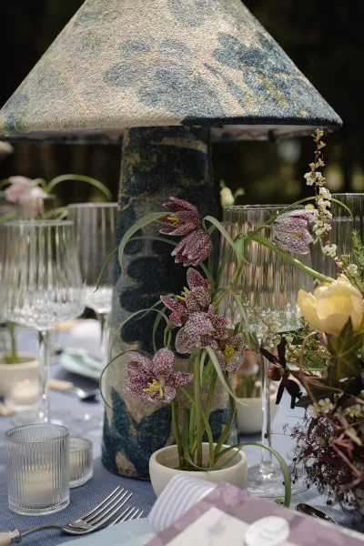 Reception tablescape with wedding table centerpiece and a patterned lamp, purple flowers and tulip, ribbed votives, in a garden setting