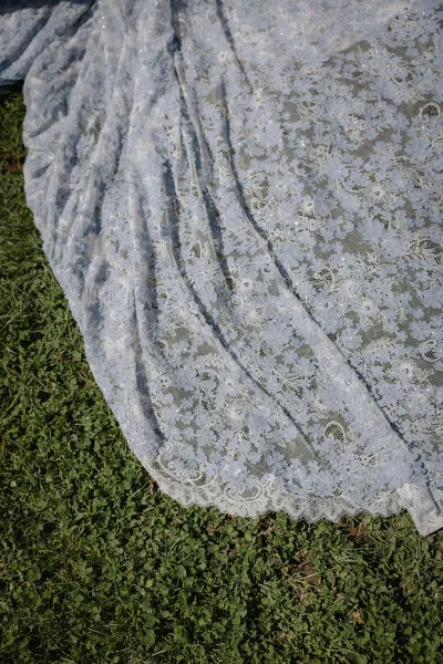 Wedding dress detail with lace wedding dress floral appliqué and subtle sequin beading, train spread across a grass lawn