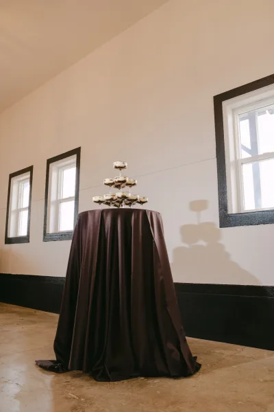 Champagne tower setup for a wedding champagne station, gleaming tiers arranged on a table with a satin tablecloth by black-trimmed windows.