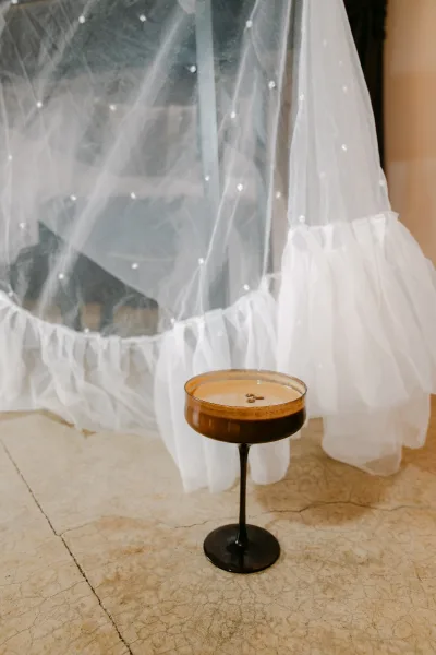 Espresso martini, a signature wedding cocktail, in a coupe glass with coffee bean garnish against a sheer tulle backdrop.