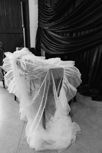 Bridal veil close-up of a pearl beaded veil spilling over a piano, delicate layers catching light against a draped fabric backdrop.