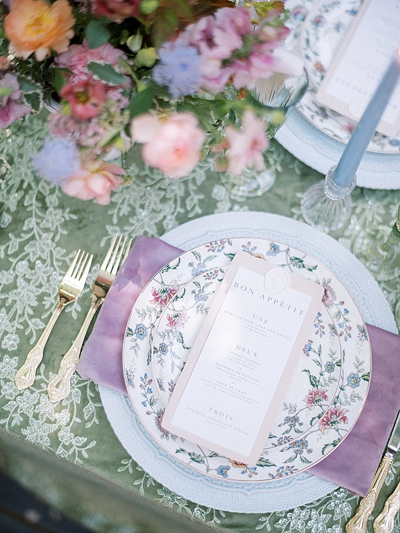 Reception tablescape wedding place setting with floral china, lavender napkin, menu card and wax seal, candles on green lace tablecloth