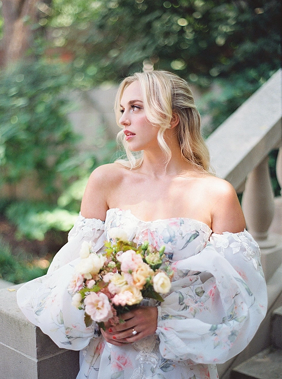 Bridal portrait of a bride in an off the shoulder wedding dress holding a pastel bouquet on outdoor steps by a stone balustrade