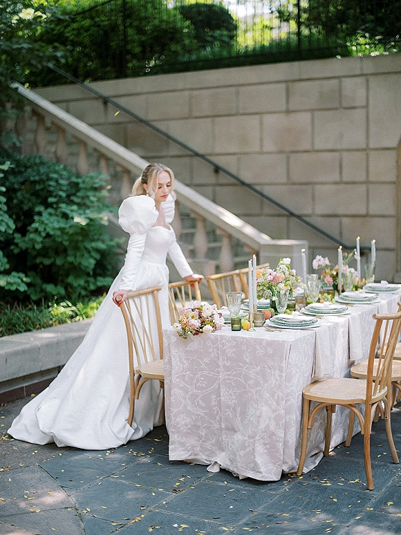 Reception tablescape with an outdoor reception table set in white linens, floral centerpieces, taper candles, and lemons on a stone patio