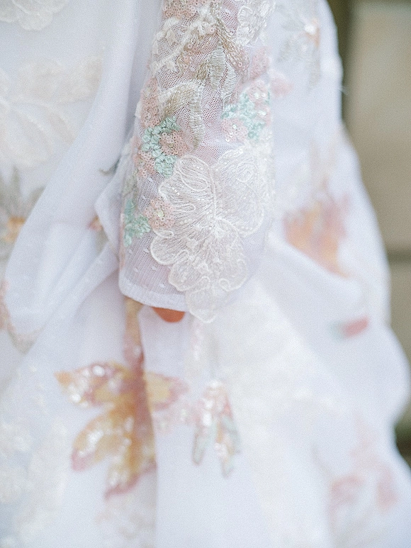 Wedding dress close-up showcasing a lace sleeve wedding dress with sheer tulle and floral embroidery, shimmering sequins against a soft neutral backdrop