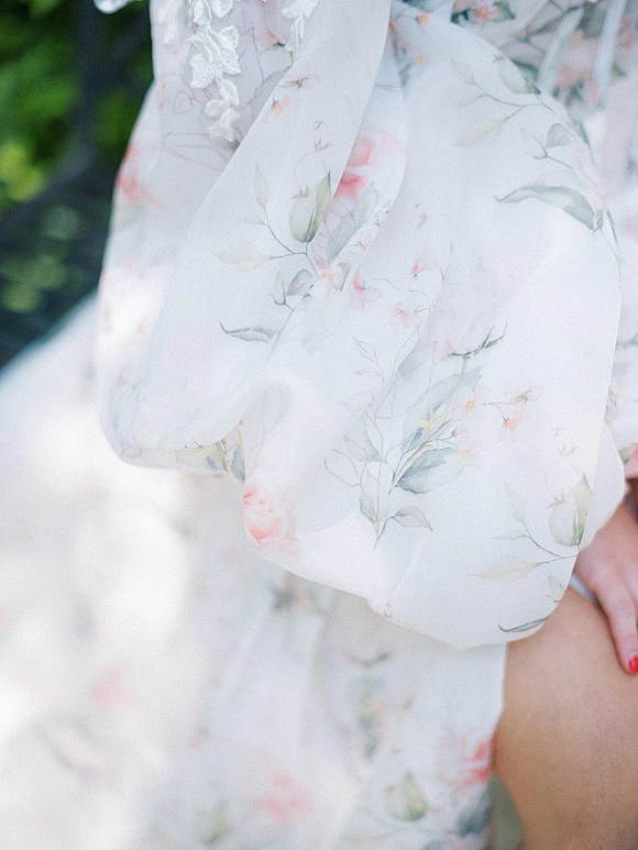 Bridal robe with soft floral print and lace trim, shown with red nail polish in soft daylight against lush outdoor greenery