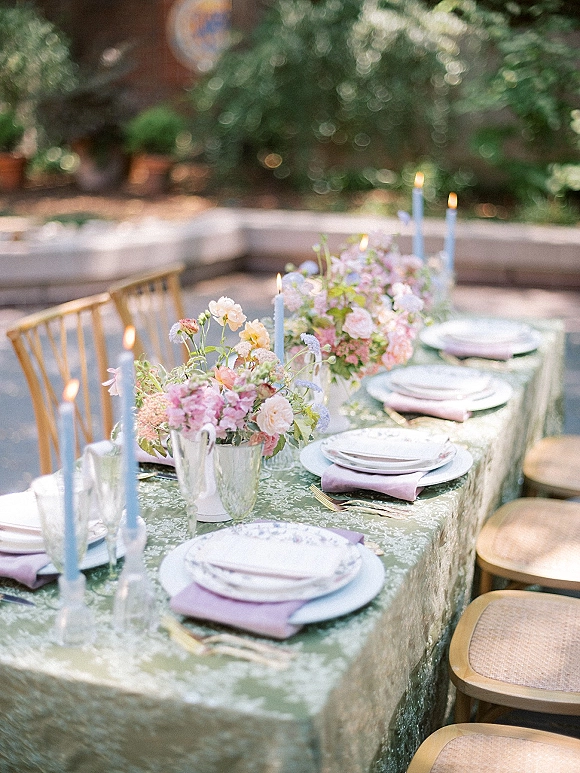 Reception tablescape with outdoor reception table styling, pastel floral centerpieces and blue taper candles on a patterned cloth in a garden patio setting