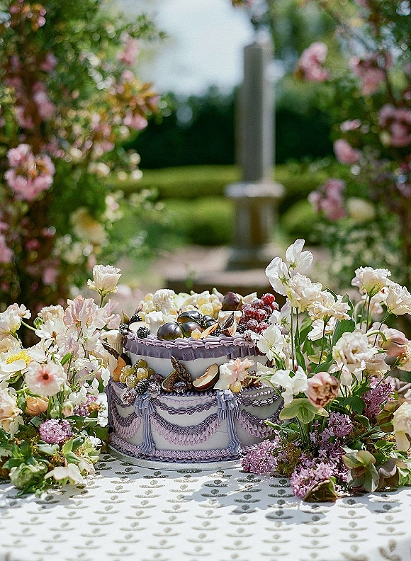 Wedding cake with fruit topped wedding cake styling, adorned with grapes, figs, berries and lavender piping on a garden table with greenery