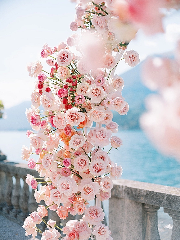 Wedding ceremony florals on a rose ceremony arch with pink roses and greenery on a white frame overlooking ocean cliffs and blue sky
