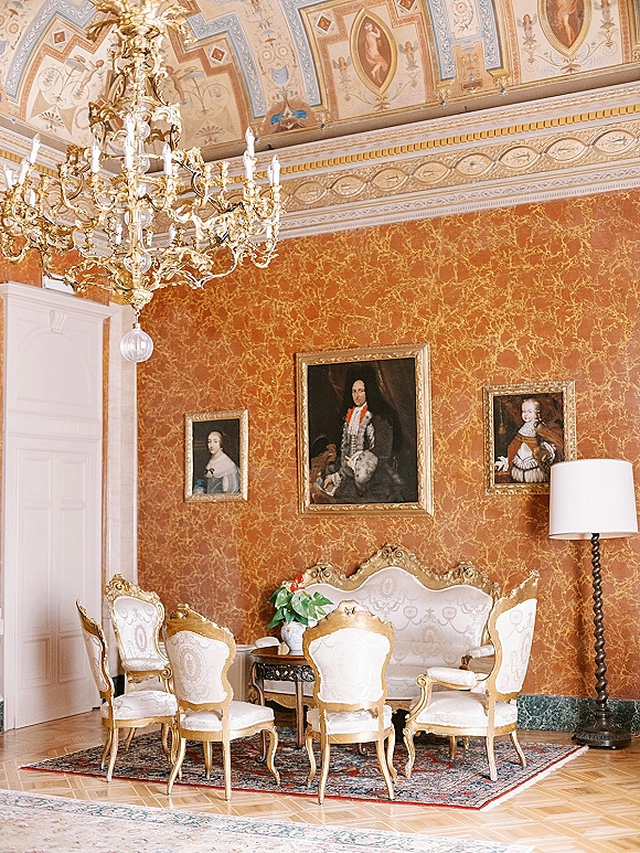 Vintage lounge seating arranged as a wedding lounge area with a gilded chandelier, settee and armchairs in a red wallpaper salon