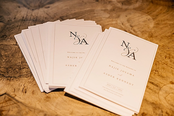 Wedding invitations with monogram wedding invitation initials in black calligraphy on white cardstock, arranged on a wood tabletop