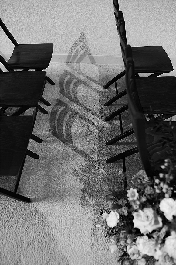 Ceremony aisle with a wedding aisle runner between rows of black chairs, ending in a floral arrangement on carpeted indoor floor