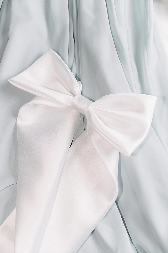 Wedding dress detail with a satin bow at the waist on a strapless bridal gown, shown in close-up against a white fabric backdrop