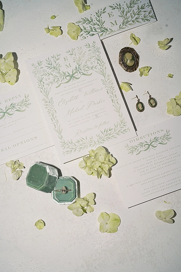 Invitation suite with wedding invitations, RSVP and details cards, sage green envelope liner, and engagement ring on a white textured surface