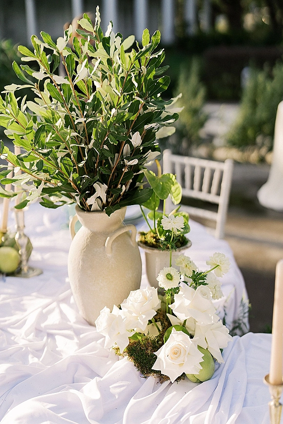 Wedding centerpiece with greenery wedding centerpiece in a ceramic pitcher vase, white roses, moss, taper candles on a sunlit garden patio table