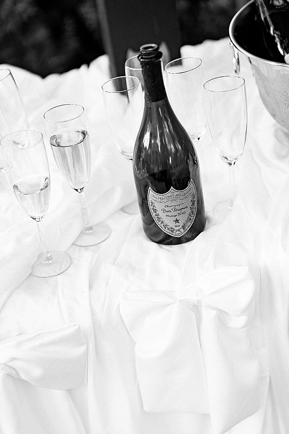 Champagne bottle at a wedding champagne toast setup with flutes and an ice bucket on a linen reception table against a dark wall
