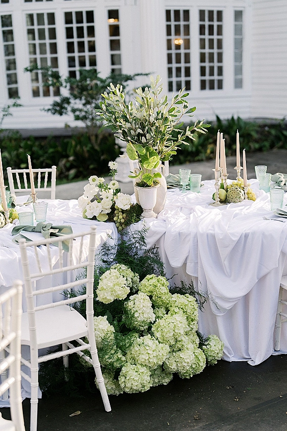 Reception tablescape with outdoor wedding tablescape styling, hydrangeas and greenery garland, taper candles, mint goblets on a patio by white windows