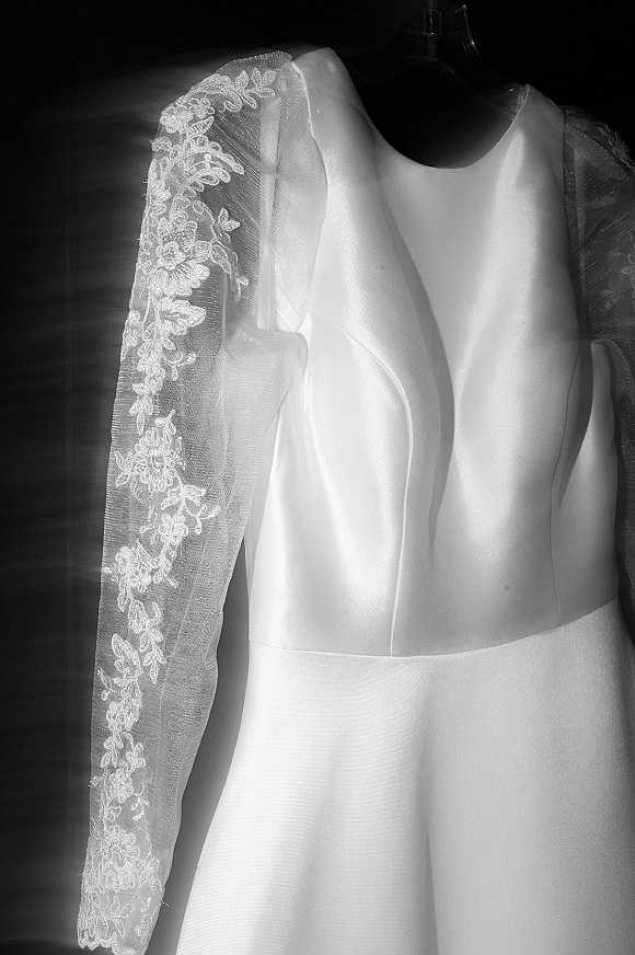 Wedding dress details featuring a lace sleeve with illusion tulle and floral applique, satin bodice and V neckline on a hanger against dark backdrop