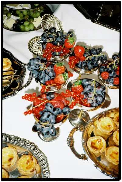 Wedding dessert table with wedding fruit cups, berry parfaits, tarts, and grapes arranged on silver trays and pedestal bowls over a white tablecloth