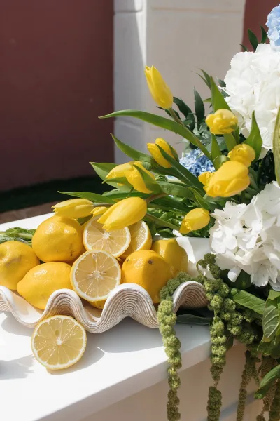 Wedding centerpiece with a lemon wedding centerpiece of yellow tulips and white hydrangeas in a ceramic shell bowl on a pedestal table in sunlight