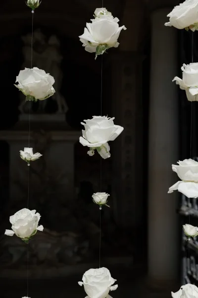 Hanging wedding flowers with hanging roses decor, white rose stems suspended by fishing line in front of a stone archway and dark doorway