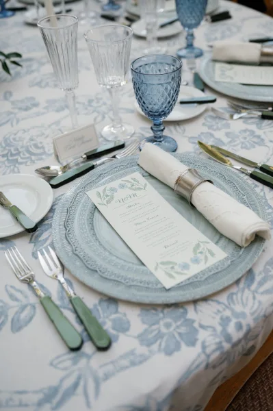 Reception tablescape with blue wedding tablescape details, layered plates on a patterned tablecloth with menus, place cards, goblets and flutes