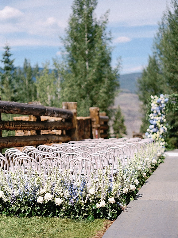 Ceremony aisle decor with blue and white aisle flowers lining an aisle runner, bentwood chairs and floral arch on a mountain lawn