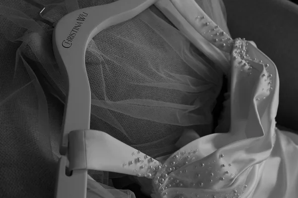 Wedding dress bridal gown detail showing pearl-beaded bodice and tulle on a hanger, draped against textured upholstered chair fabric