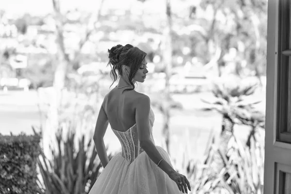 Bridal portrait in black and white of bride in a strapless lace corset gown, side profile by window light with blurred garden foliage outside