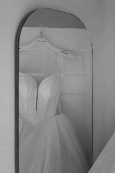 Wedding dress on hanger with lace bodice and spaghetti straps reflected in a mirror against a white paneled door