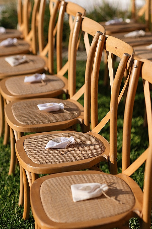 Ceremony seating with wood folding chairs wedding arranged in rows on a grass lawn, featuring linen favor bags tied with twine