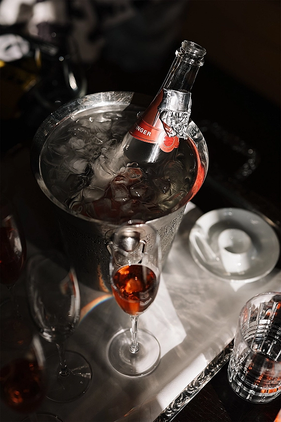 Champagne bottle in ice bucket beside a champagne flute, water glass, and espresso cup on a tabletop in a dark room