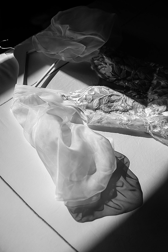 Wedding dress detail with floral lace appliqué on sheer tulle straps, softly lit with shadows across the fabric surface